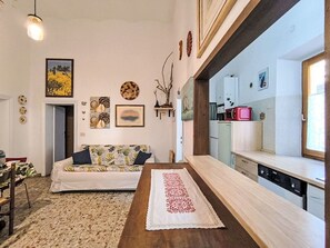Uma sala de estar com sofá, mesa de centro e área de cozinha com eletrodomésticos.
