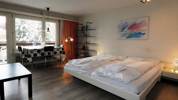 A modern bedroom with a large bed, a desk, and a chair. There is a window with curtains, a bookshelf, and a painting on the wall. - Sarazena Appartement/Fewo 2-Bettwohnung H by Interhome (Saas-Fee)