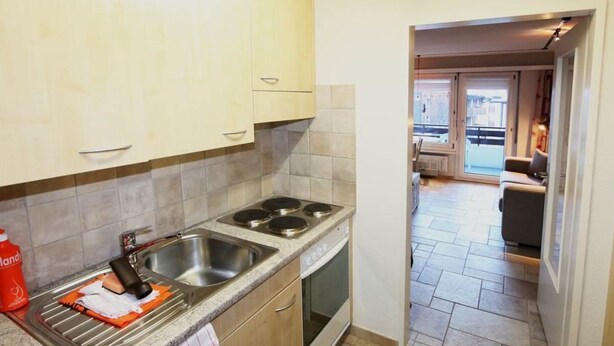 A kitchen with a double sink, a stove, and a view of the living area through an open door. - Sarazena Appartement/Fewo 2-Bettwohnung O by Interhome (Saas-Fee)