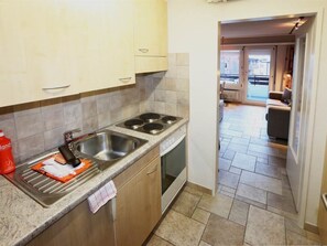 A kitchen with a double sink, a stove, and a view of the living area through an open door. - Sarazena Appartement/Fewo 2-Bettwohnung O by Interhome (Saas-Fee)
