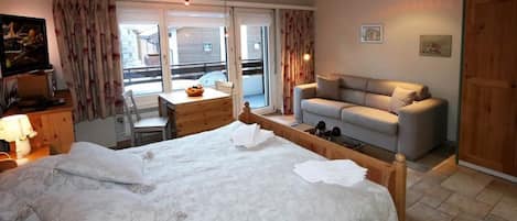 A bedroom with a bed, a desk, a sofa, and a window.