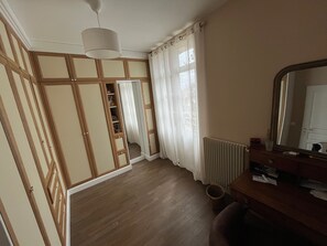 Et værelse med et træskab, et spejl, en radiator og et vindue med gardiner.