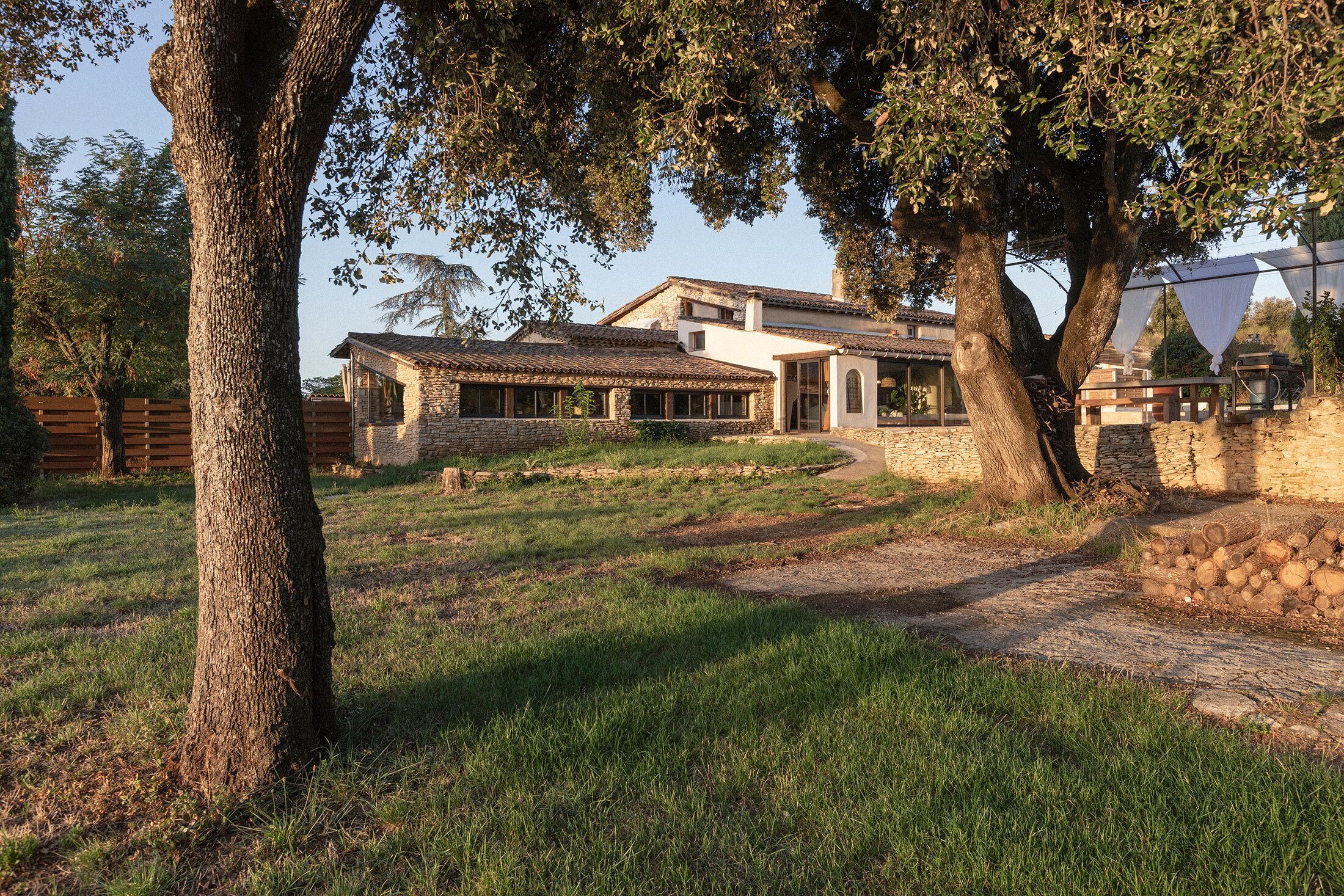 Une maison en pierre avec un toit de tuiles, entourée d’arbres et d’une pelouse.