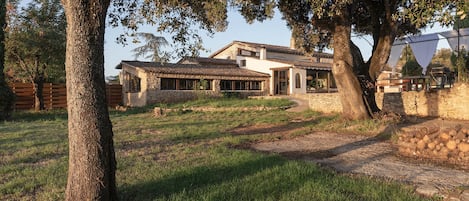 Una casa de piedra con techo de tejas, rodeada de árboles y un césped.