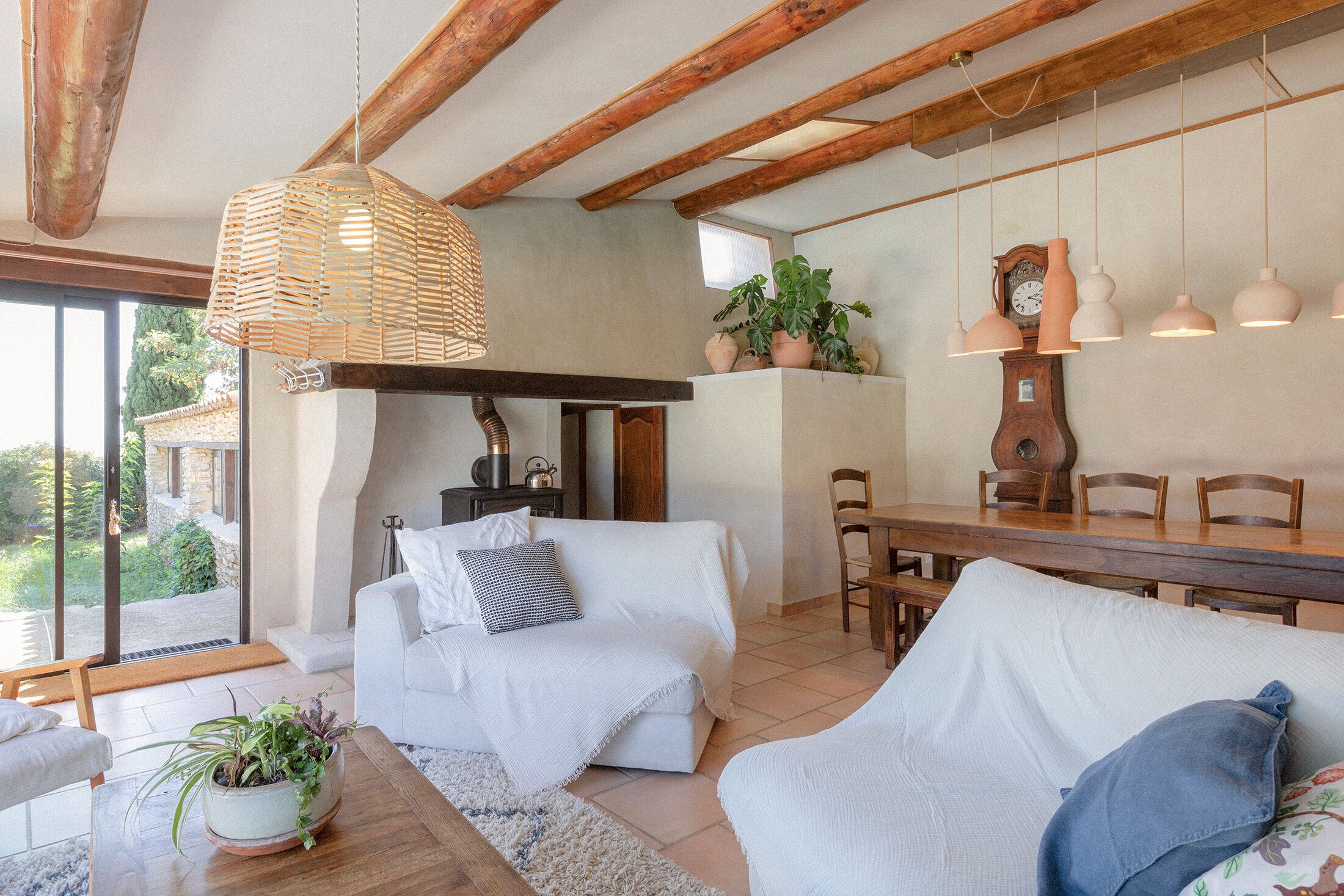 Een gezellige woonkamer met een witte bank, een houten eettafel en een hangende, geweven lamp.