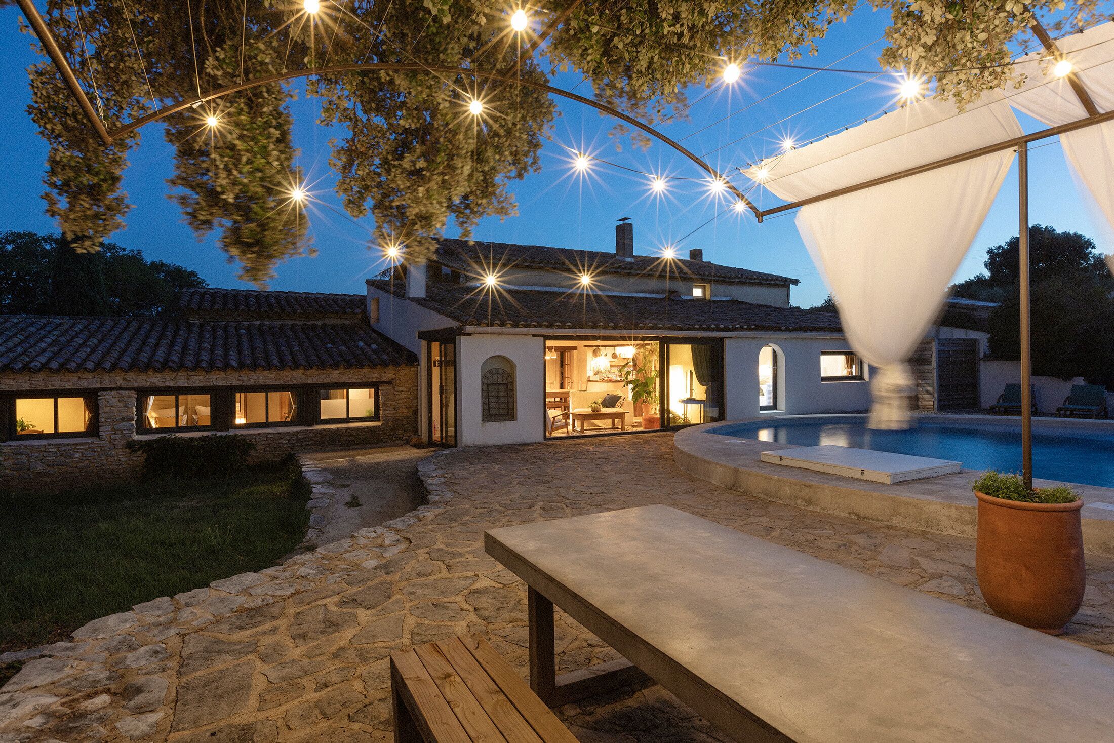 Una casa de fachada de piedra, piscina y luces colgantes.