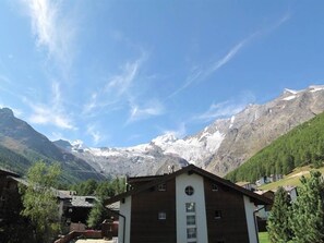 Ein Bergdorf mit traditionellen Holzhäusern, blauem Himmel und schneebedeckten Gipfeln im Hintergrund.