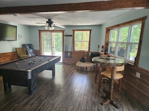 A pool table with balls, a billiards table, a ceiling fan, and windows with a view of greenery.
