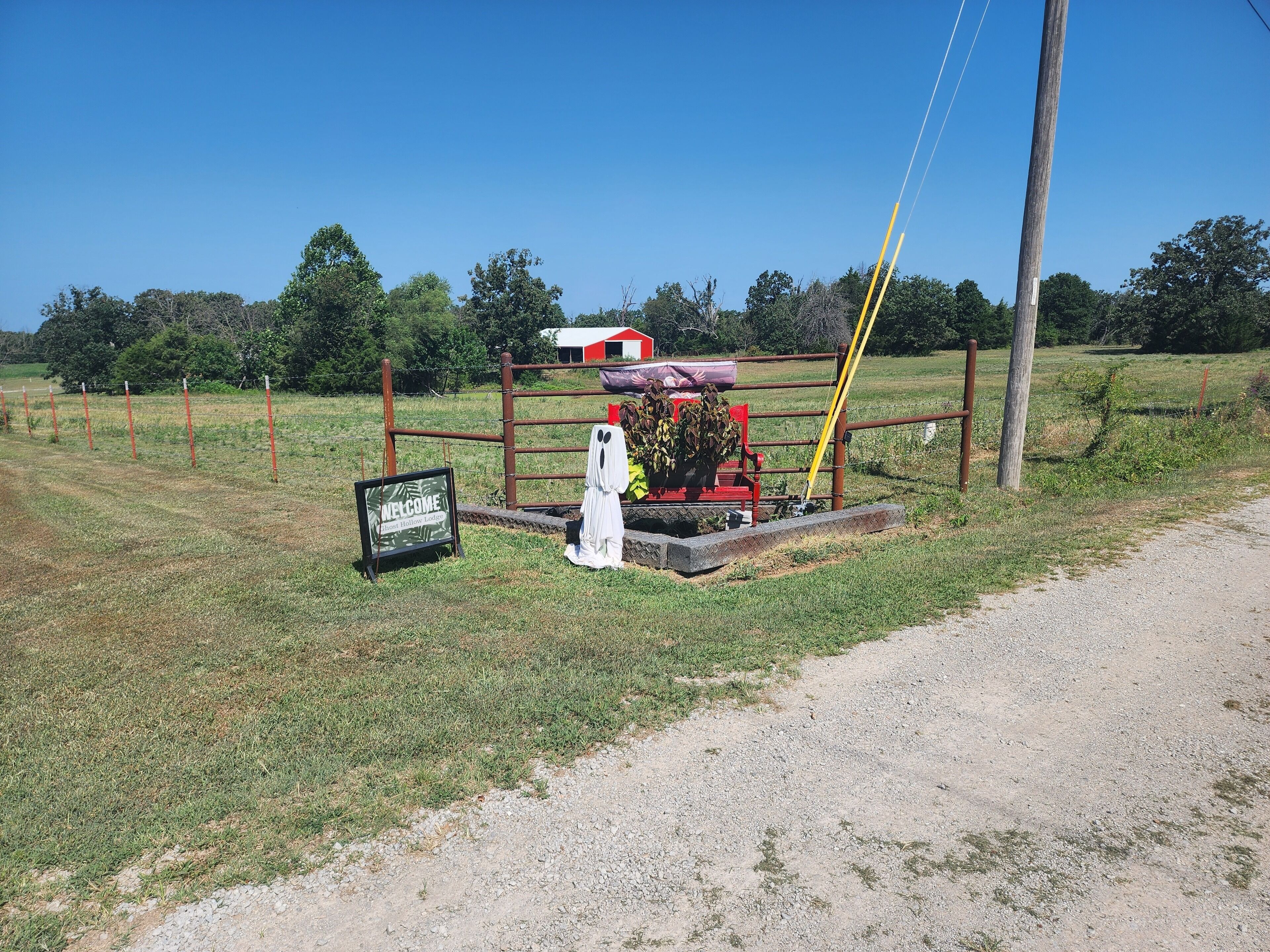 A rural landscape with a dirt road, a metal gate, and a welcome sign.