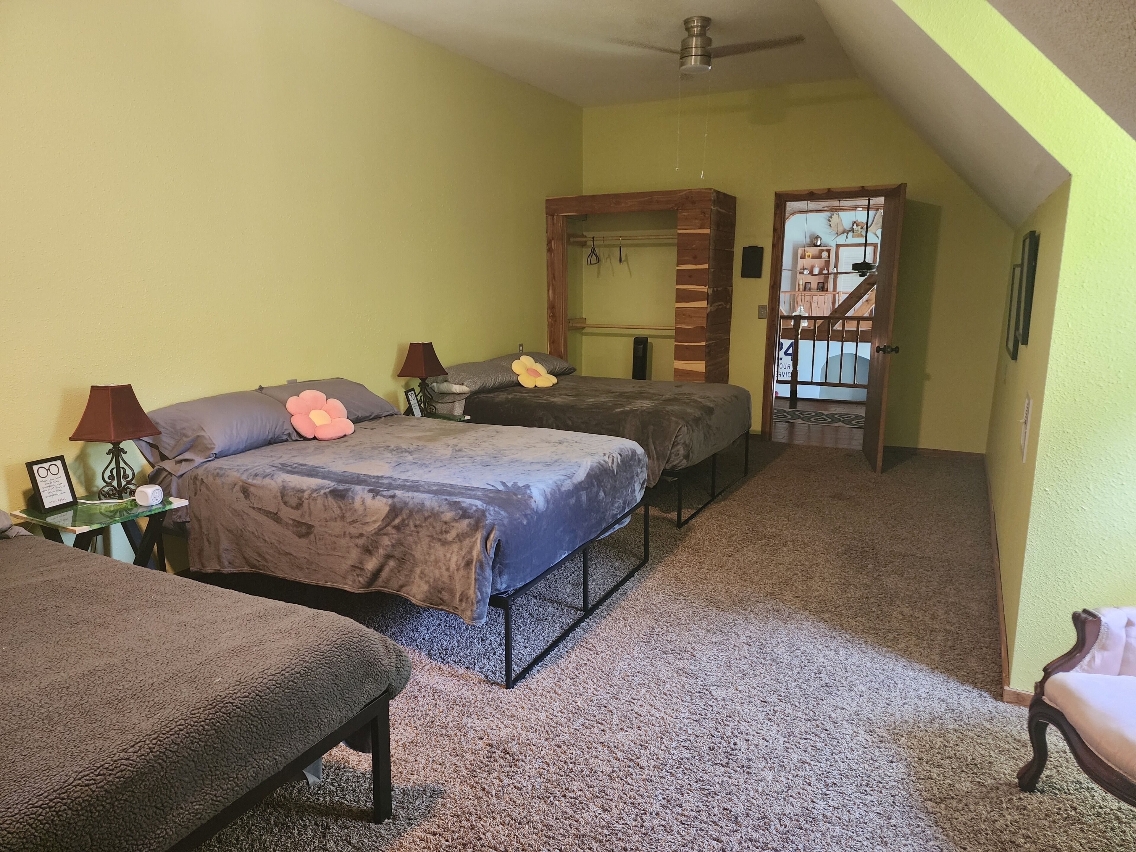 Quarto com duas camas, ventoinha no teto, porta de madeira e chão coberto de carpete.