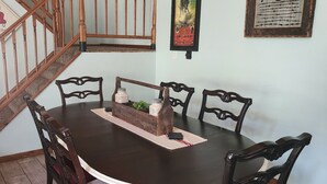 Un coin repas avec une table ronde, six chaises, un escalier en bois et deux affiches encadrées au mur.