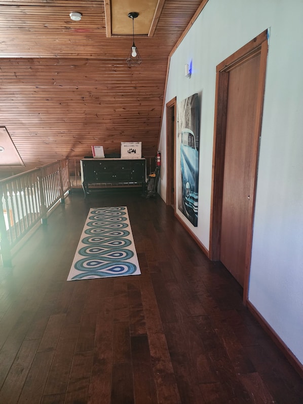 A wooden-floored hallway with a decorative rug, a reception desk, and a wall-mounted light fixture.