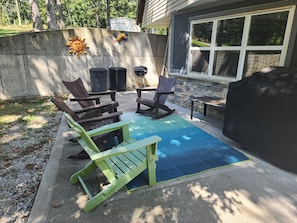 An outdoor patio with a blue mat, two rocking chairs, a table, and a grill.