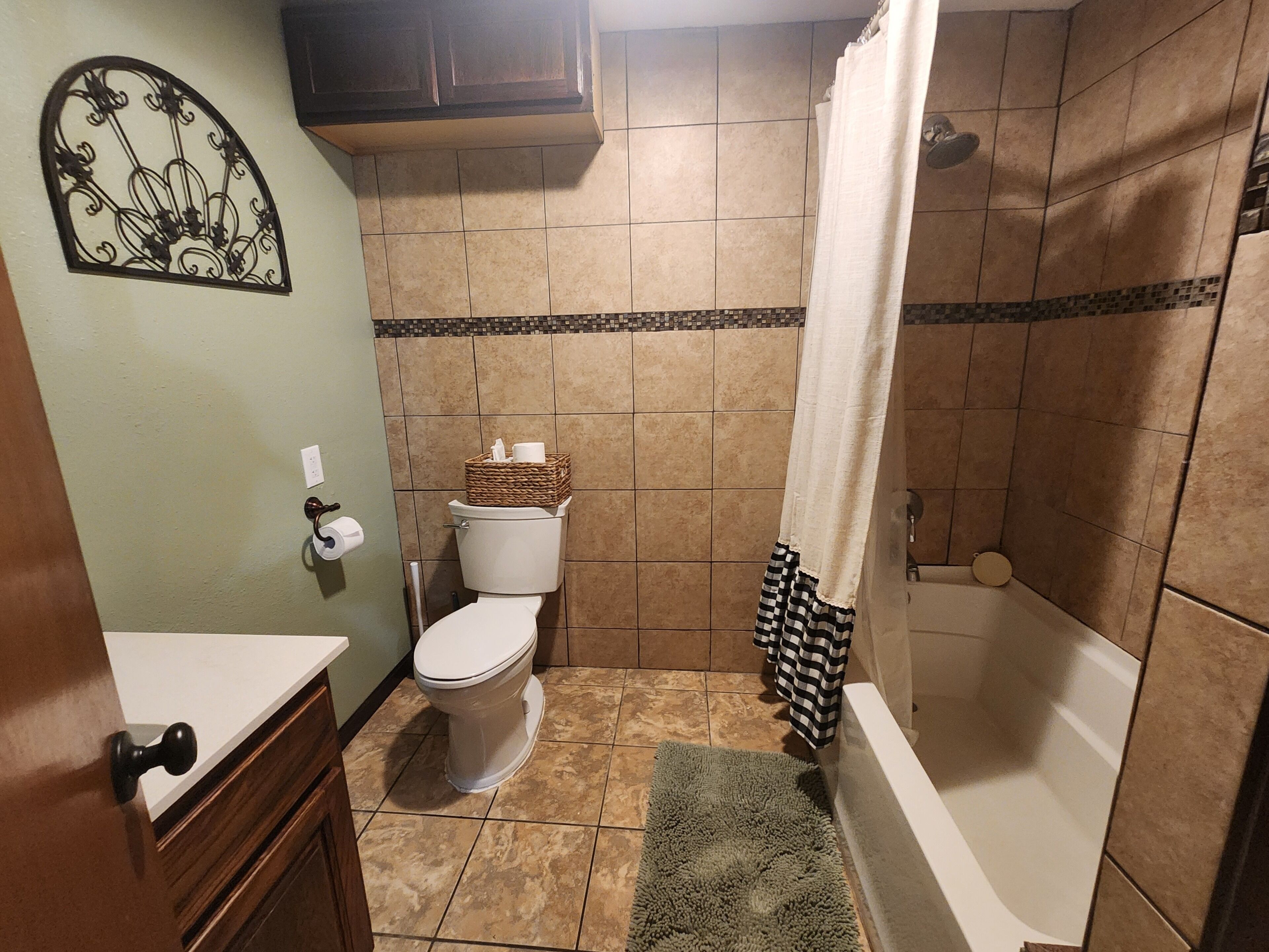 A bathroom with a toilet, a shower with a curtain, a sink, and a decorative wall piece.
