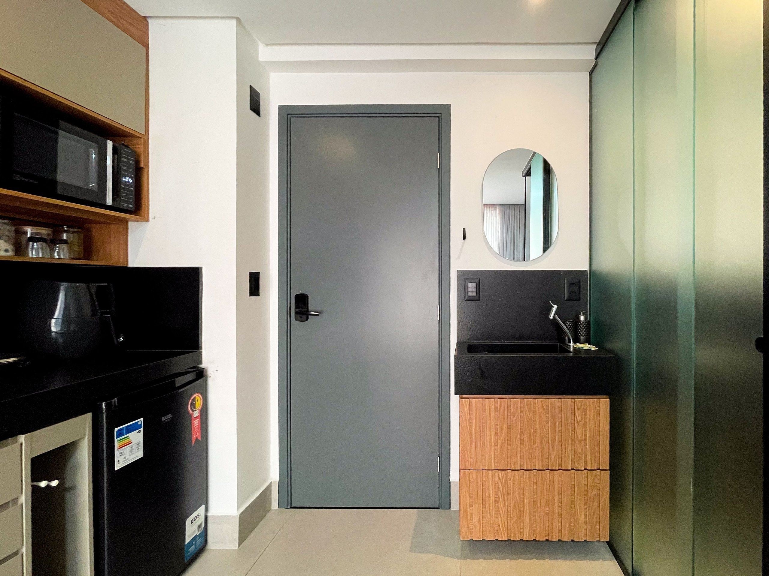 Una kitchenette compacta con microondas, cafetera y lavamanos con un espejo arriba.