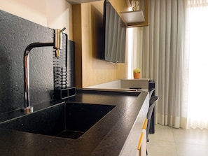 A modern kitchen with a black countertop, stainless steel faucet, and a built-in oven. - Get By Side By Hosppedar (João Pessoa)