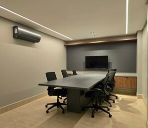 A conference room with a long table, chairs, a flat-screen TV, and a wall-mounted air conditioning unit. - Get By Side By Hosppedar (João Pessoa)