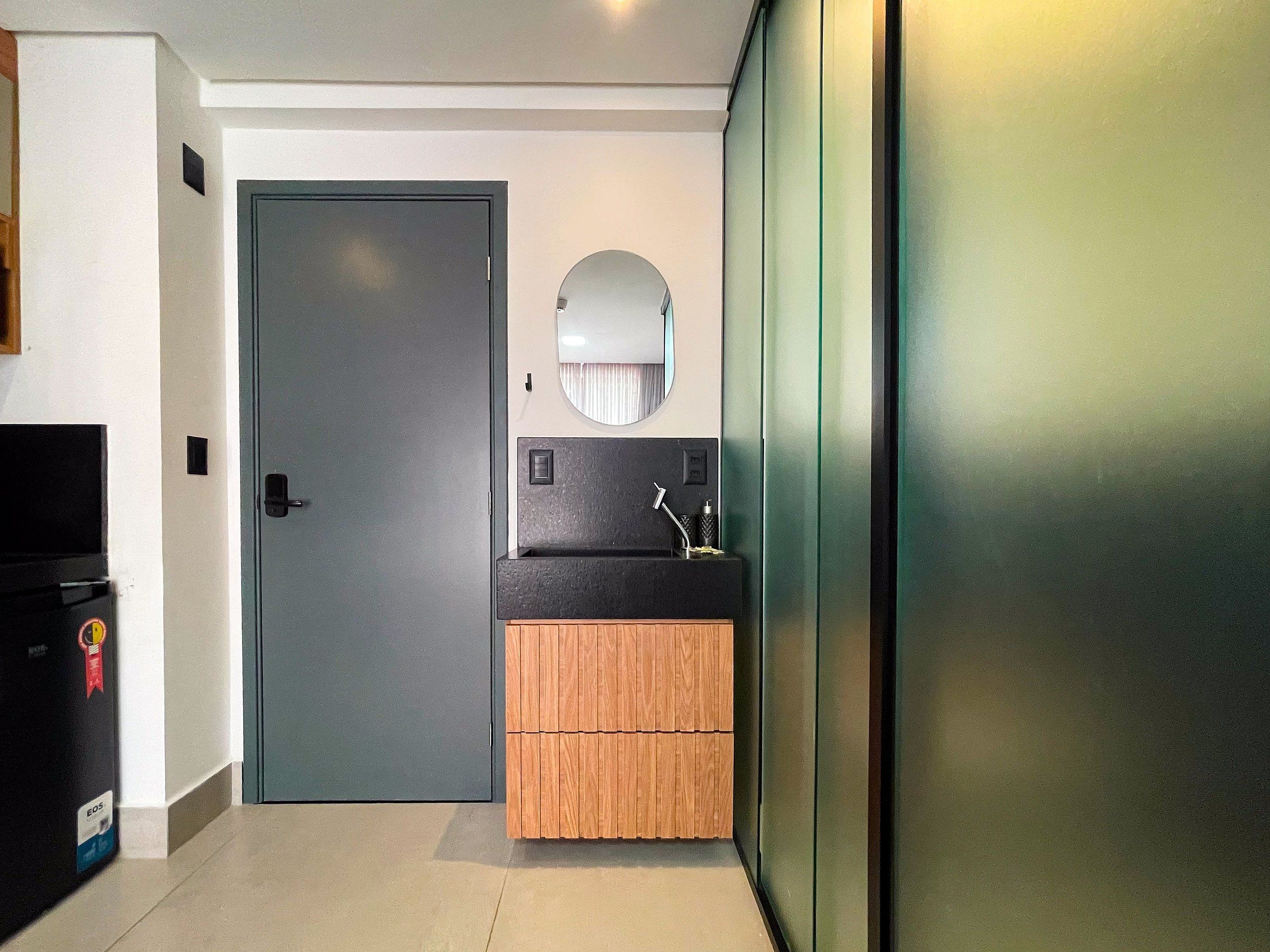 Un baño pequeño con una puerta gris, un lavamanos con un espejo encima y un mueble de madera abajo.