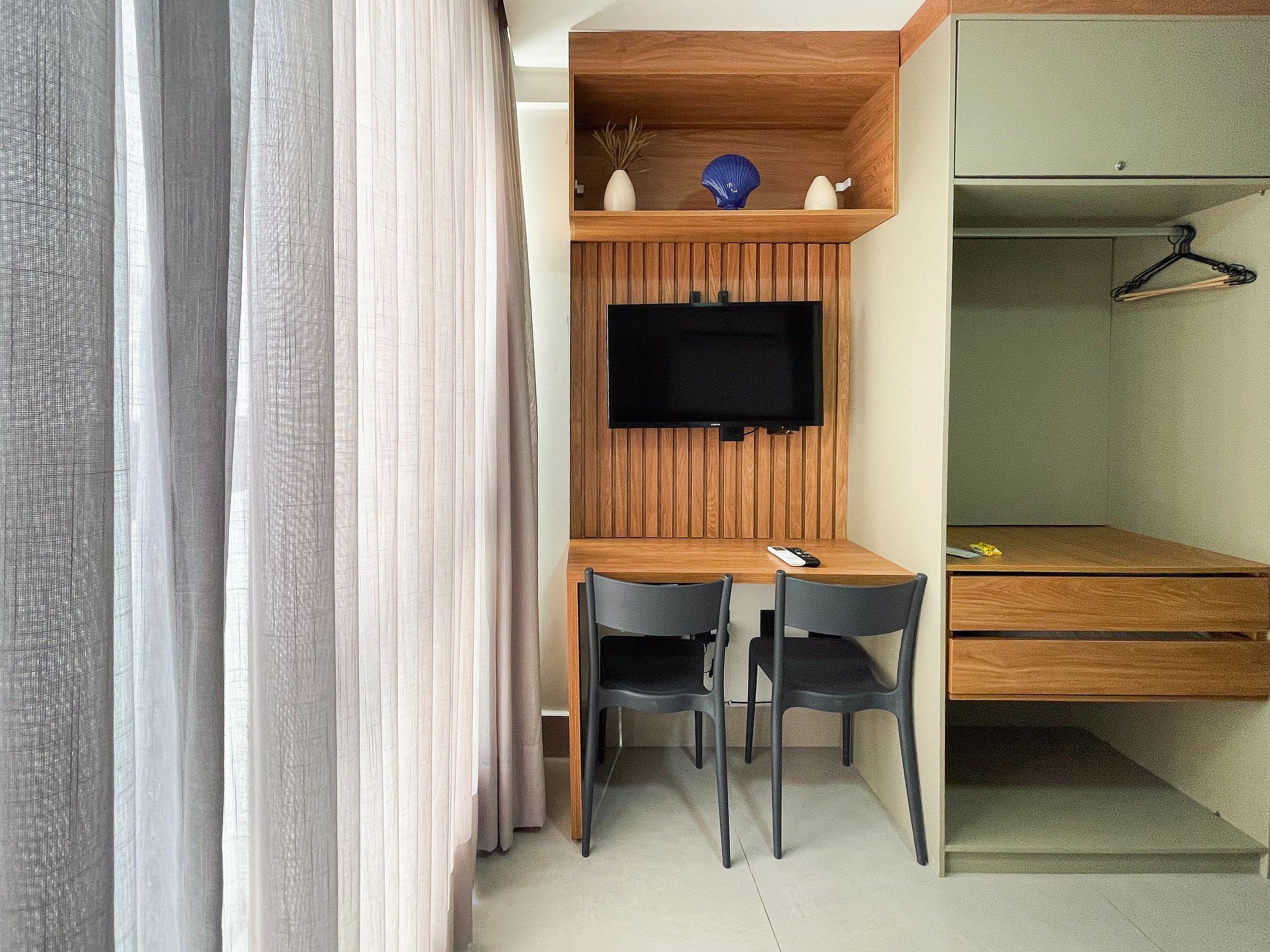 Une pièce de taille modeste, avec un bureau en bois, deux chaises, un téléviseur fixé au mur et une armoire avec un cintre.