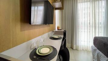 Habitación de hotel con una mesa de comedor para dos, un televisor de pantalla plana en la pared y una cama con colcha a rayas.