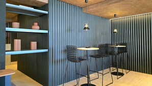 Un interior moderno con techo de madera, pared azul con líneas verticales y una silla de metal negro con una mesa redonda.
