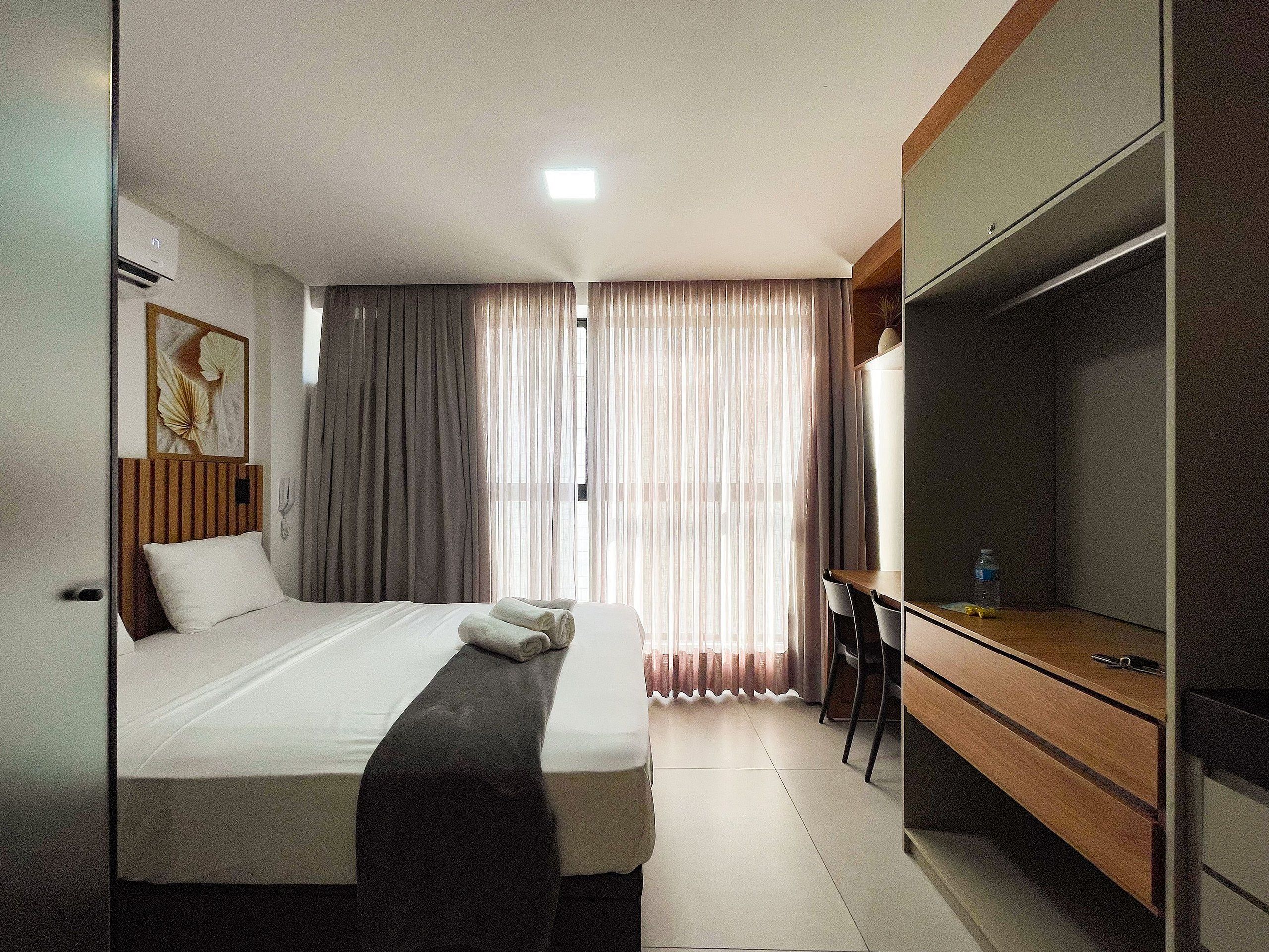 A hotel room with a bed, a desk, a television, and a window with curtains.