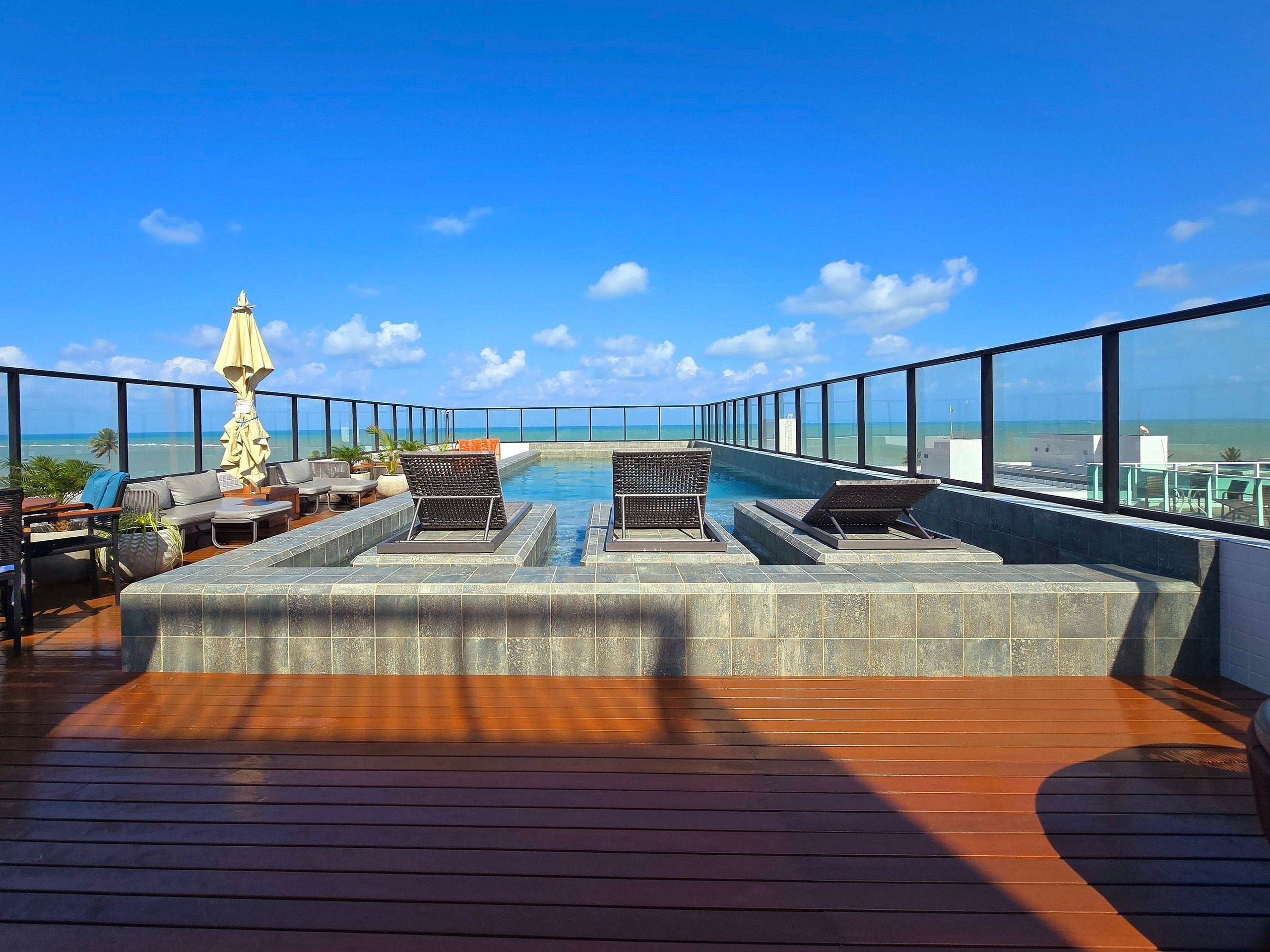 Área de piscina no terraço com espreguiçadeiras e vista para o mar.