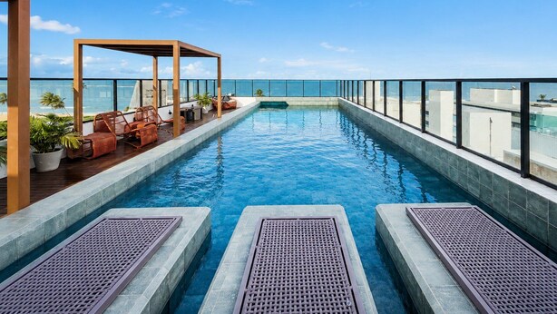 Piscina infinita en la azotea con una pérgola de madera y sillones de descanso con vistas al océano.