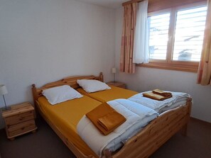 Ein Einzelzimmer mit Holz-Kopfteil, einem Nachttisch mit Lampe und einem Vorhangfenster.