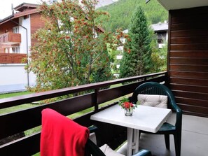 A balcony with a table and chairs, a red chair, and a view of a mountain and buildings. - Sarazena Appartement/Fewo 4-Bettwohnung E by Interhome (Saas-Fee)