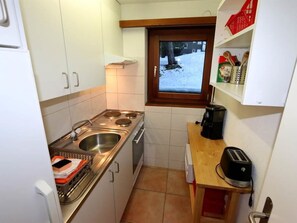 A compact kitchen with a stove, sink, and a window overlooking a snowy landscape. - Sarazena Appartement/Fewo 4-Bettwohnung E by Interhome (Saas-Fee)