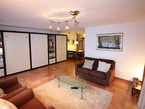A living room with a brown sofa, a glass coffee table, and a white rug. There is a bookshelf and a dining area in the background. - Sarazena Appartement/Fewo 4-Bettwohnung E by Interhome (Saas-Fee)