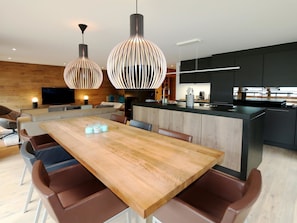 Eine moderne Küche mit einer zentralen Kochinsel, einem Holzespeisetisch und Pendelleuchten.
