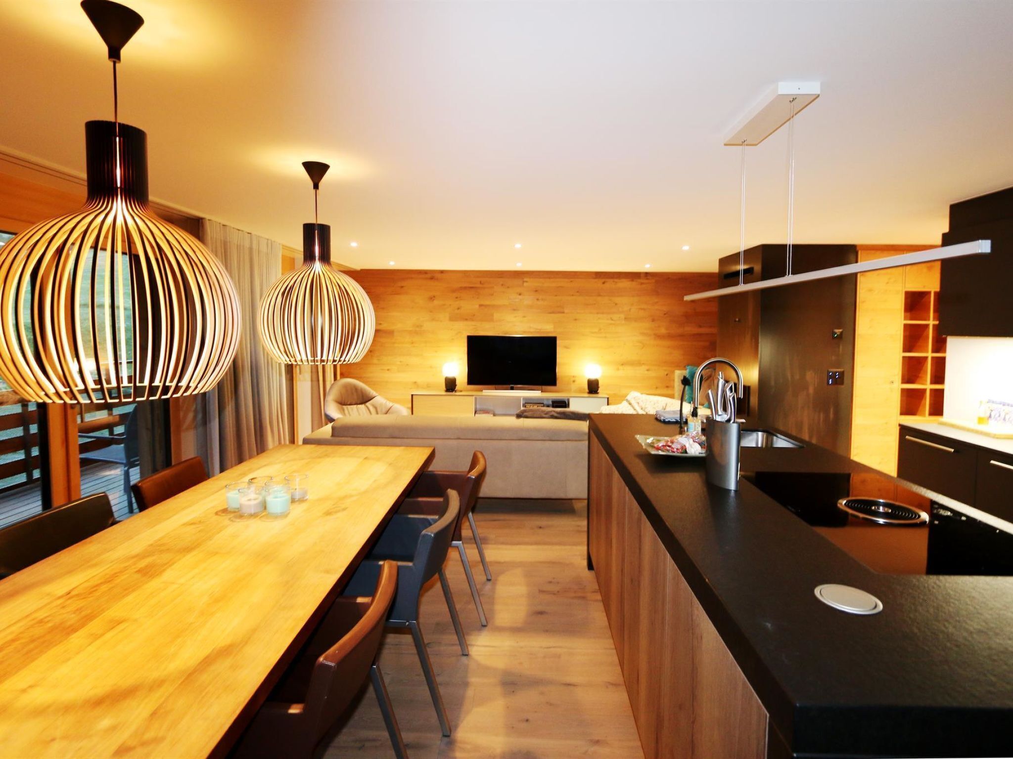 A modern kitchen with a wooden island, a dining area with a long table and chairs, and pendant lighting.