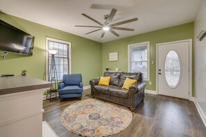 A living room with a ceiling fan, a blue armchair, a brown leather sofa with yellow cushions, a patterned rug, and a television mounted on the wall. - Blue Haven in Erwin, TN (Erwin)