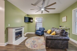 A living room with a fireplace, a leather sofa, a blue armchair, a round rug, and a ceiling fan. - Blue Haven in Erwin, TN (Erwin)