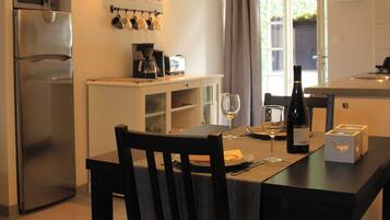 Een eethoek met een tafel voor twee personen, een koffiezetapparaat en een fles wijn.