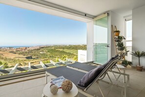 A balcony with a view of a green landscape and a distant town. - Casa Panorama Cortesin, luxury apartment with ocean and golf course views (Casares)