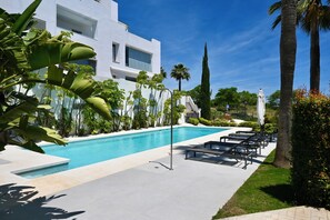 Ein moderner Poolbereich mit einem klaren, blauen Pool, Liegestühlen und tropischen Pflanzen.