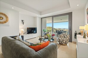 A modern living room with a grey sofa, a television, a coffee table with flowers, and a patterned armchair. - Casa Panorama Cortesin, luxury apartment with ocean and golf course views (Casares)