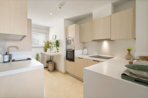 A modern kitchen with a sink, stove, microwave, and cabinets. - Casa Panorama Cortesin, luxury apartment with ocean and golf course views (Casares)