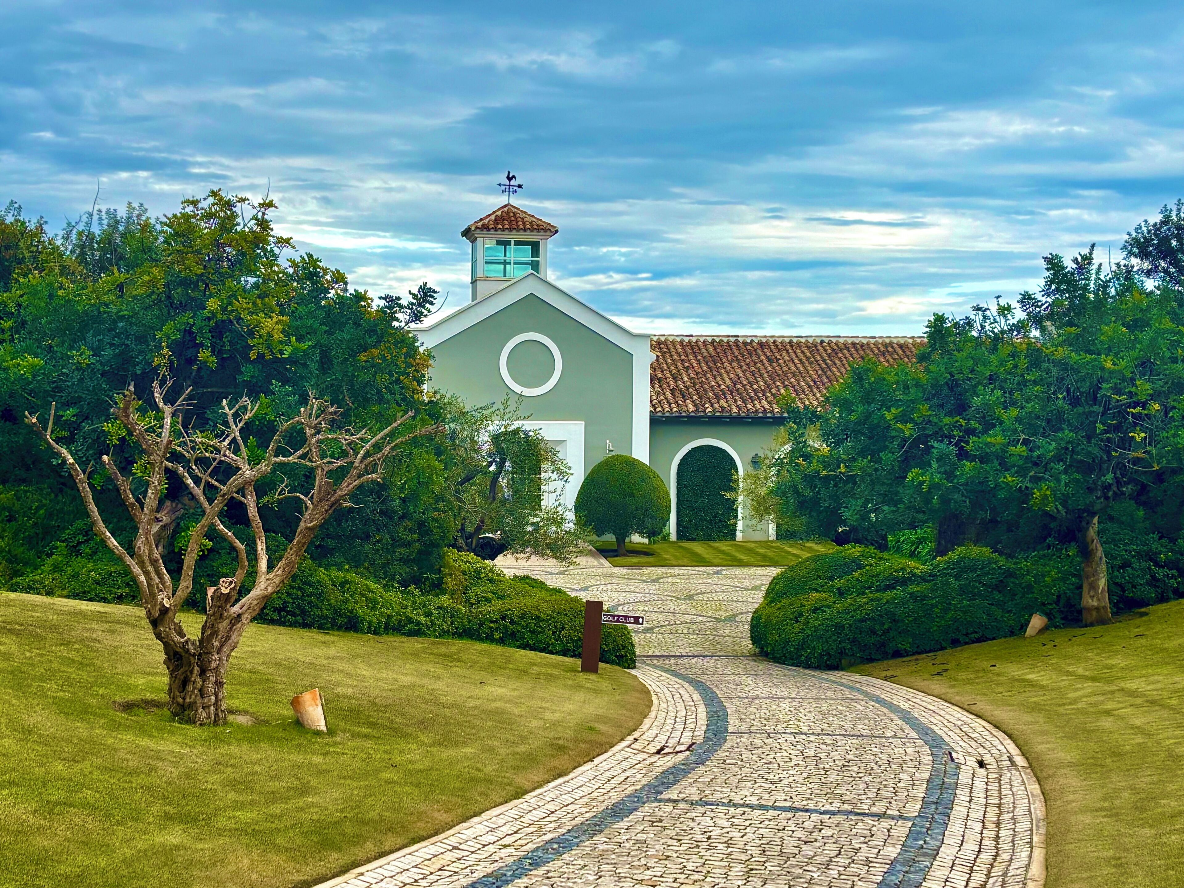 A building with a circular window and a tower, surrounded by well-maintained grass and trees.