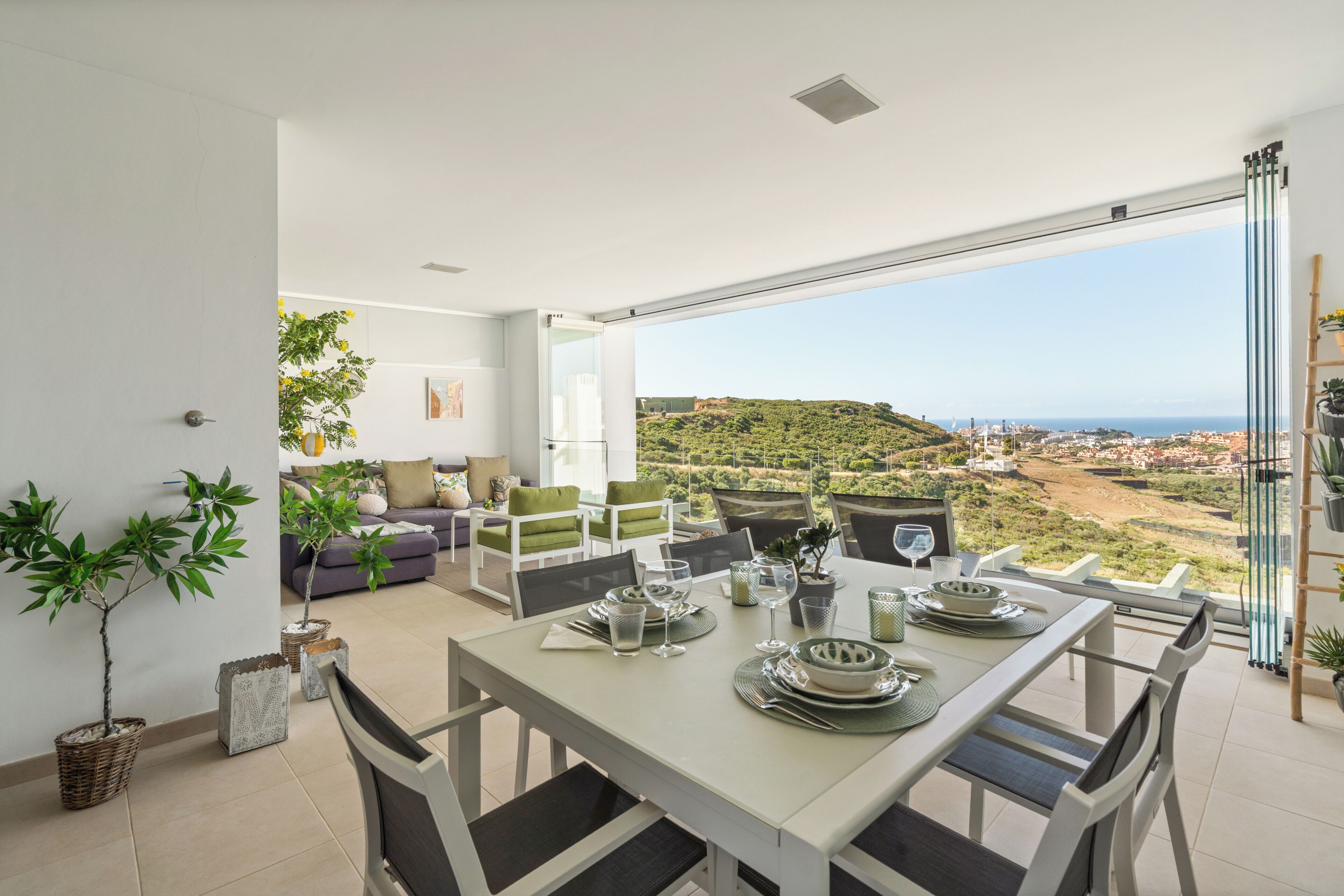 Un comedor con una mesa dispuesta para cuatro personas, un sofá y vistas a un paisaje montañoso.