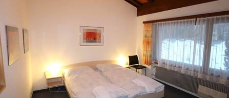 Habitación de hotel con cama, lámparas de noche, radiador y ventana con cortinas.