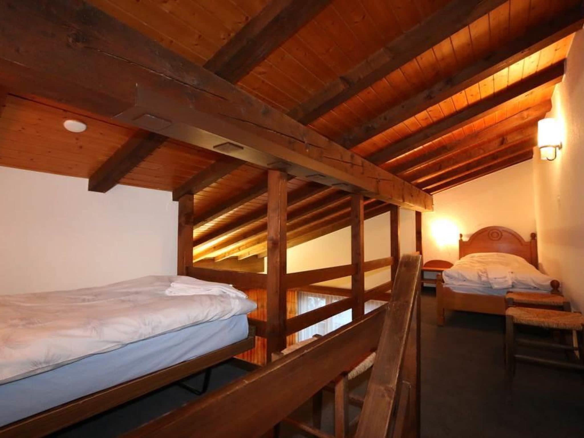 Une chambre de dortoir avec des lits superposés en bois et un lit simple, des poutres en bois au plafond et un luminaire fixé au mur.