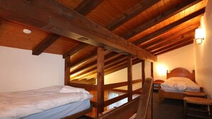 Ein Schlafraum mit Holzbettkästen, einem Einzelbett, Holzbalken an der Decke und einer wandmontierten Leuchte.