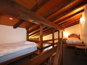 A dormitory room with wooden bunk beds and a single bed, wooden beams on the ceiling, and a wall-mounted light fixture. - Sarazena Appartement/Fewo 4-Bettwohnung U by Interhome (Saas-Fee)