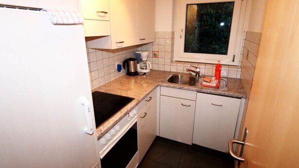 Eine kompakte Küche mit weißen Schränken, einem eingebauten Backofen, einer Kaffeemaschine und einem Fenster über der Spüle.