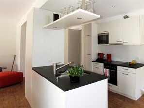 A modern kitchen with white cabinets, a black countertop, and a small island with a sink and plant. - Dolomit Appartement/Fewo, Dusche und Bad, WC, 2 Schlafräume 5-Bettwohnung EG by Interhome (Saas-Fee)