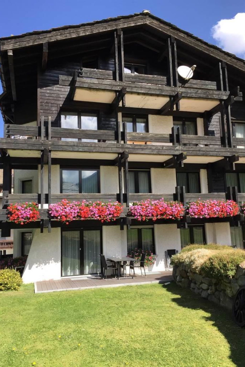 A multi-story building with balconies, a covered outdoor seating area, and a stone wall.